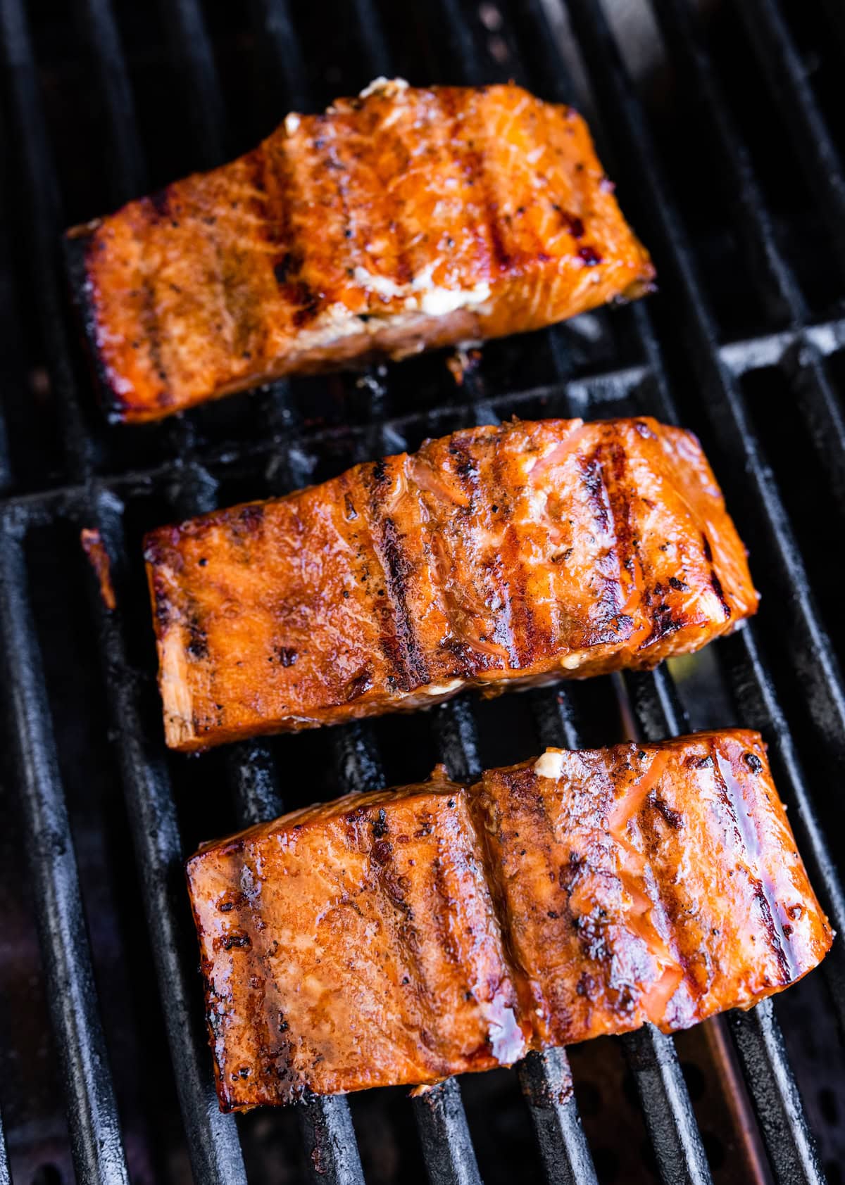 Three grilled salmon filets on a grill.