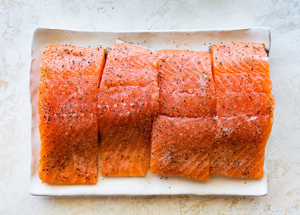 Four seasoned and raw salmon filets on a plate.