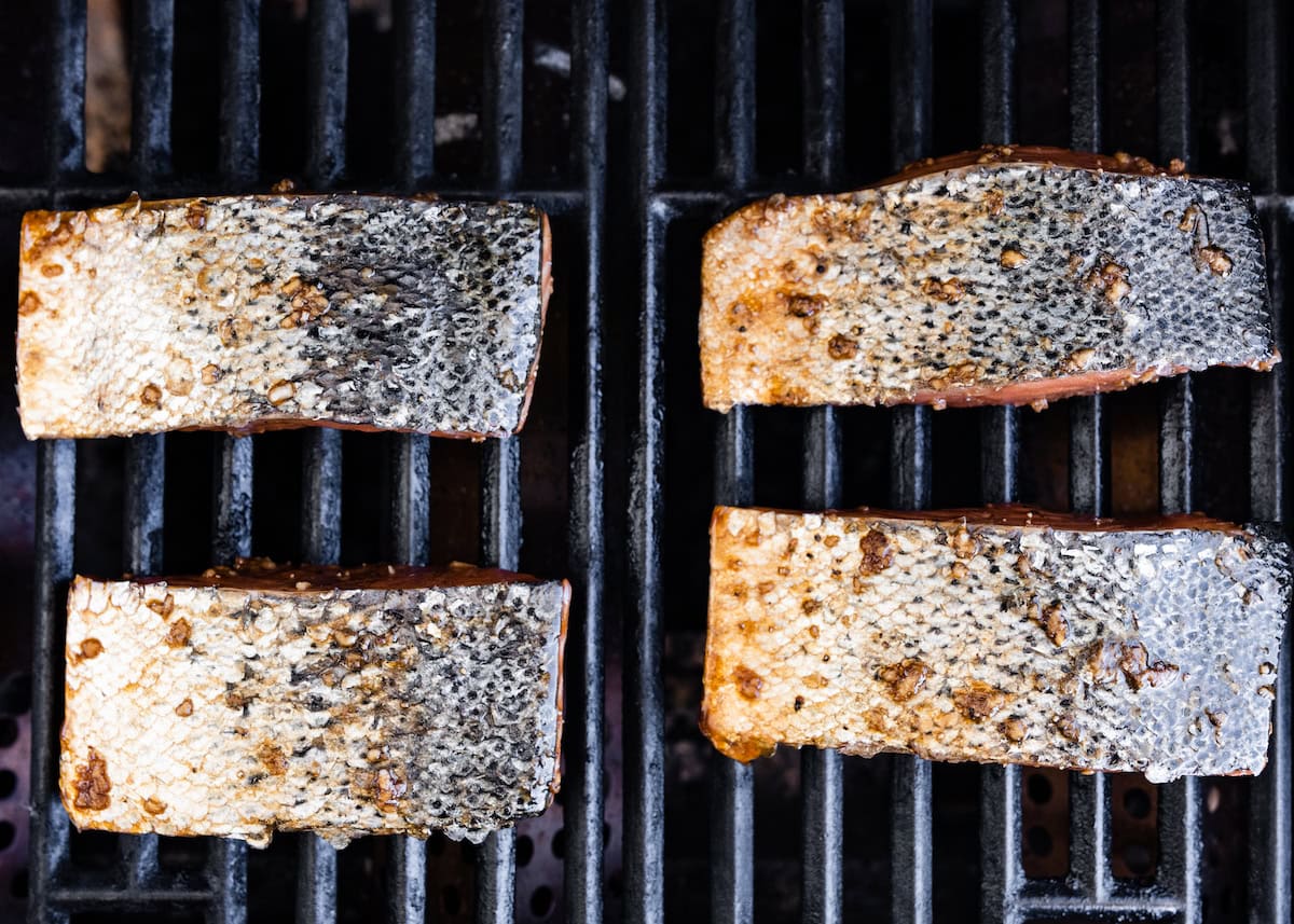 Four salmon filets on the grill with the skin of the salmon facing up.