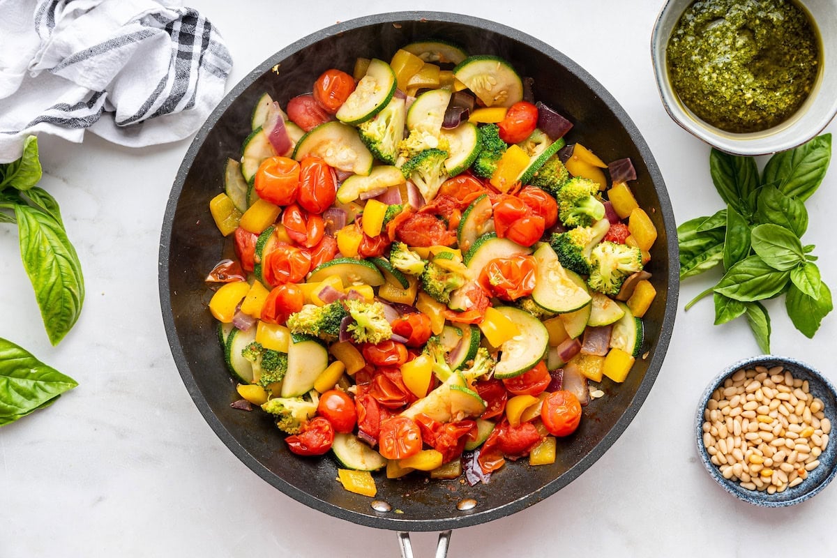 A large skillet of cooked vegetables including cherry tomatoes, broccoli, bell pepper, and zucchini.
