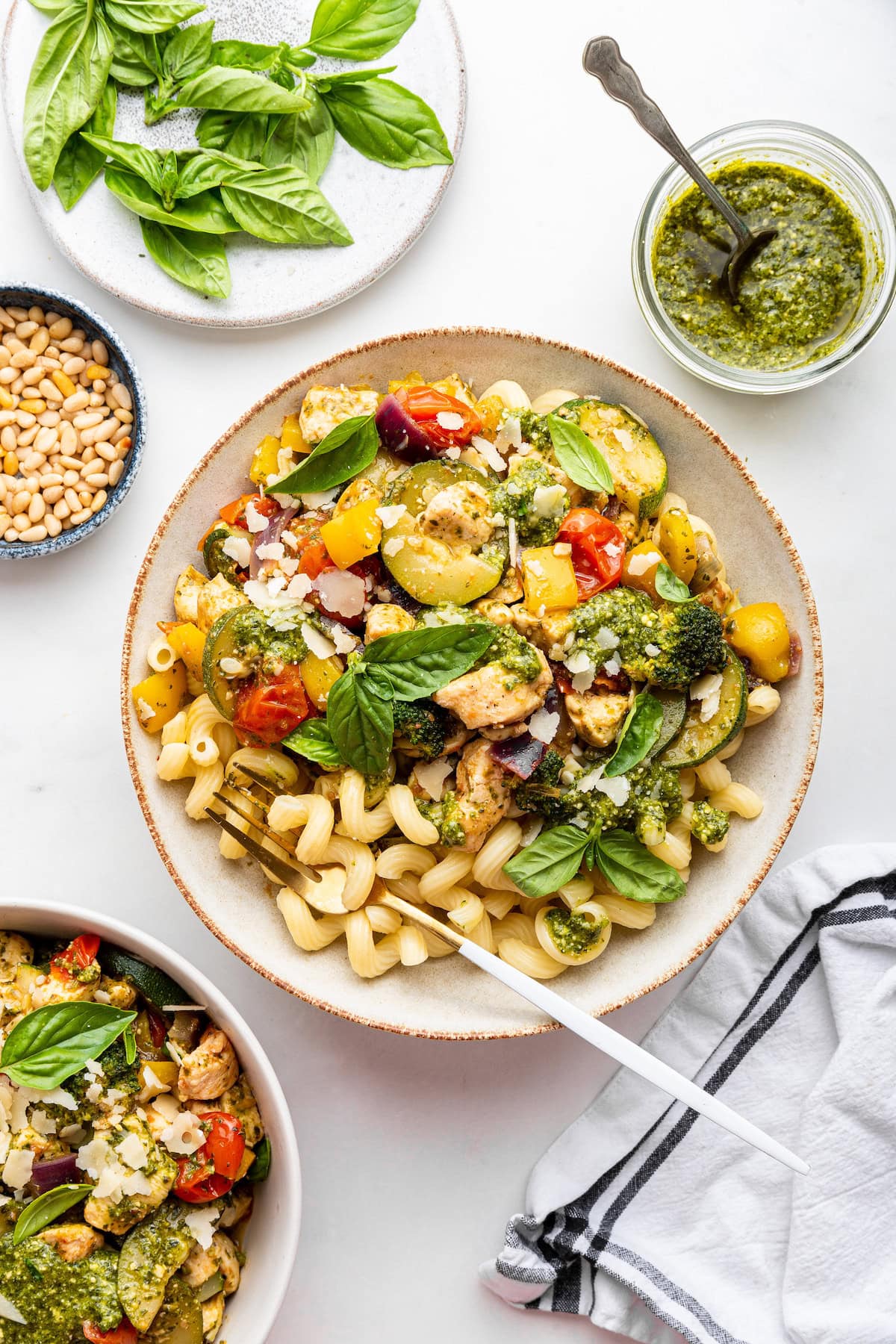 A plate of pesto chicken served with vegetables, pasta, and fresh basil.