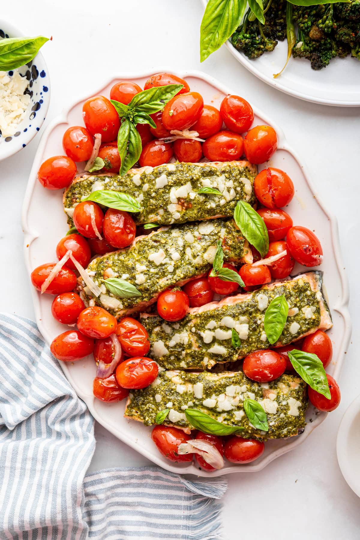 Four salmon filets covered in pesto and surrounded by cherry tomatoes on a large plate.