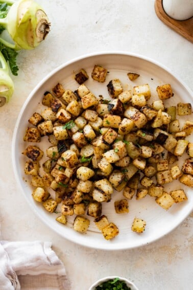 A plate of seasoned and roasted kohlrabi with a kohlrabi root near the plate.