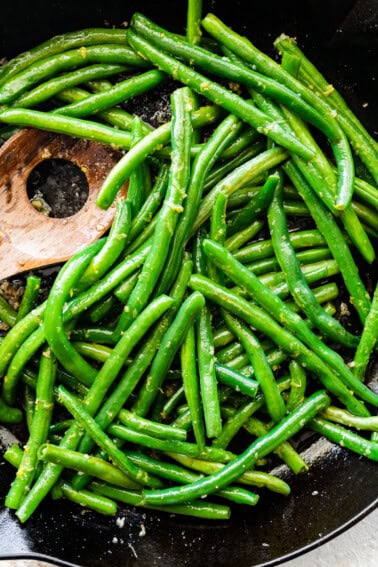 Sautéed Green Beans in a skillet with a wooden spatula.