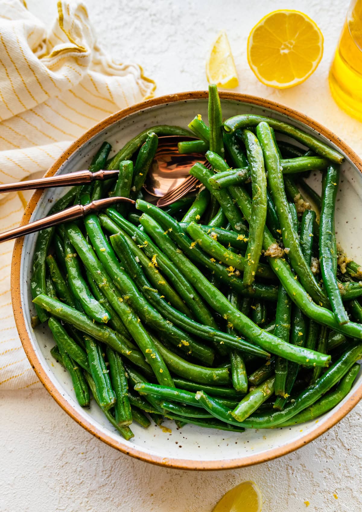 Sautéed green beans in a large bowl with a metal spoon and fork.
