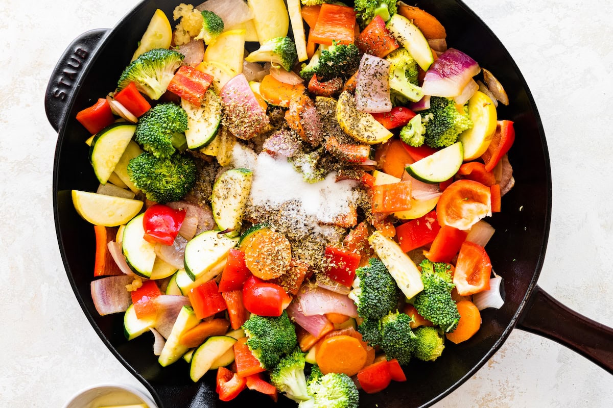 A cast iron skillet with uncooked vegetables and seasonings.