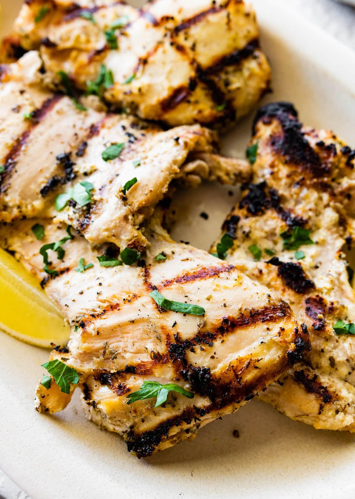 Multiple yogurt marinated chicken thighs on a plate garnished with fresh herbs.