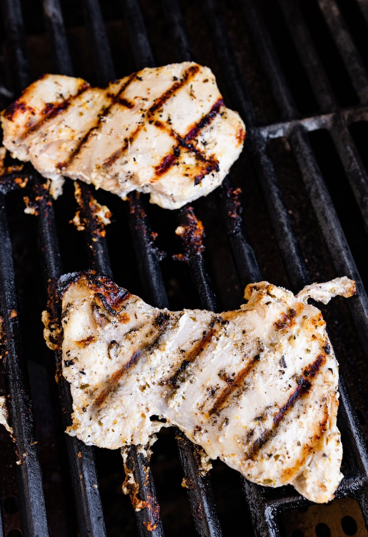 Two yogurt marinated chicken thighs cooking on a grill.
