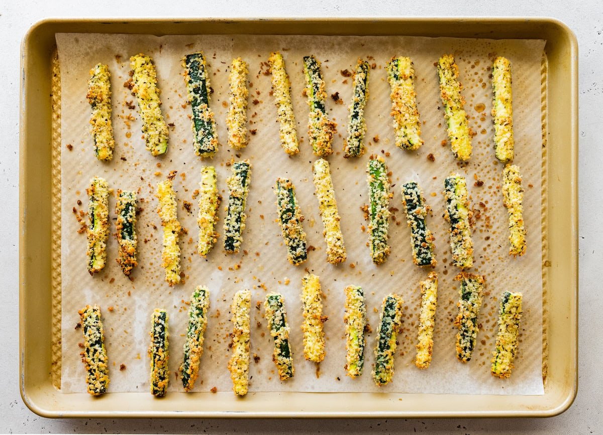 A large baking tray full of crispy zucchini fries covered in panko bread crumbs.
