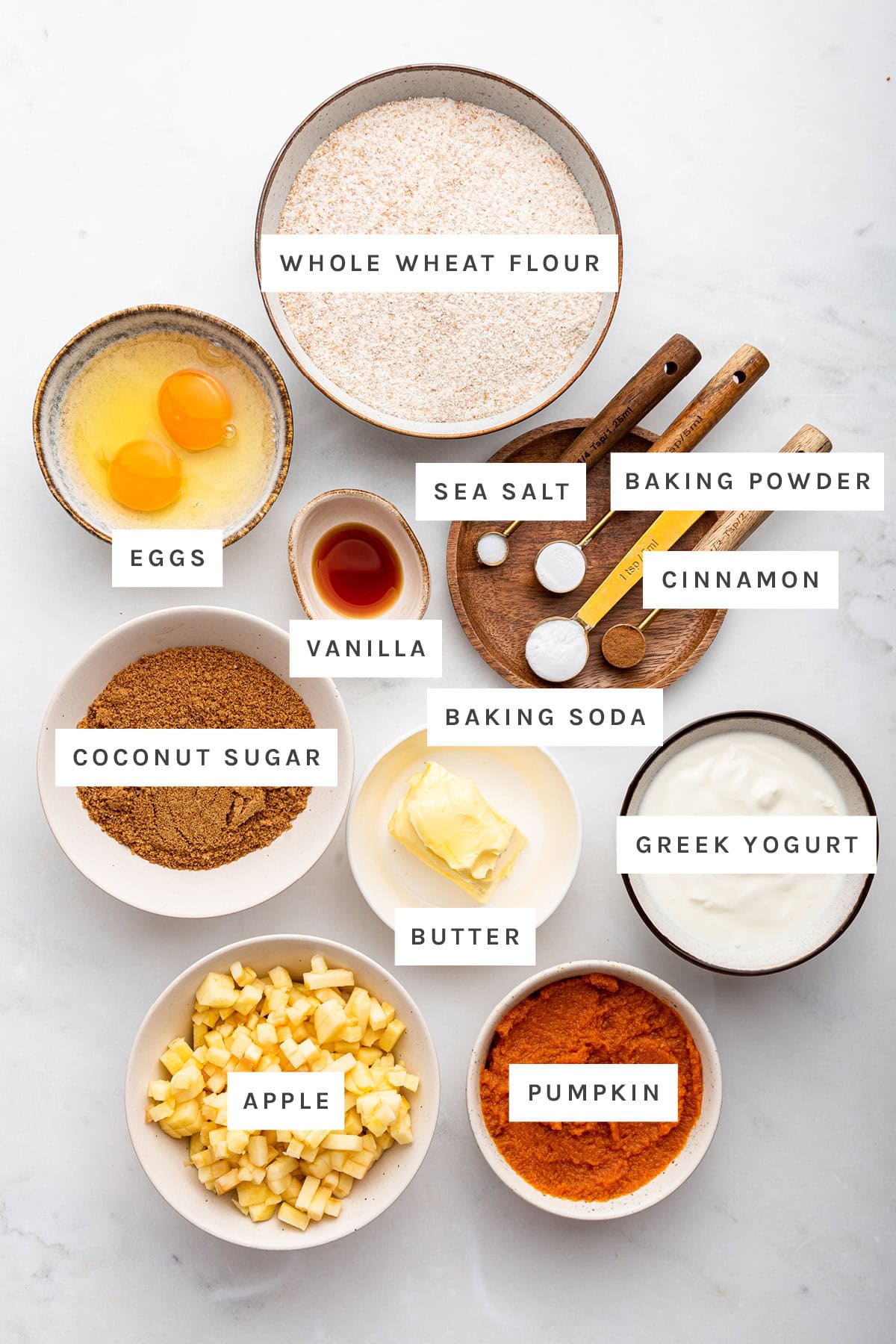 Ingredients measured out to make Healthy Apple Cinnamon Muffins: whole wheat flour, eggs, vanilla, sea salt, baking powder, cinnamon, baking soda, coconut sugar, butter, Greek yogurt, apple and pumpkin.