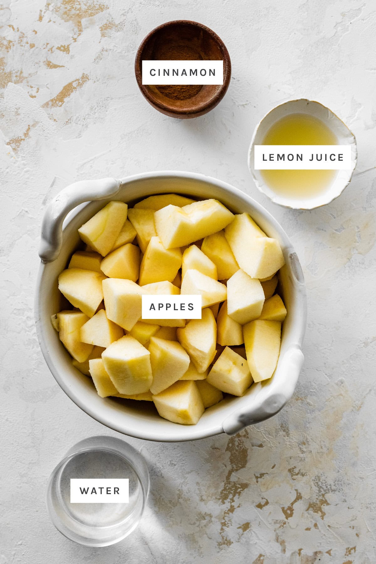 Ingredients measured out to make Homemade Applesauce: cinnamon, lemon juice, apples and water.