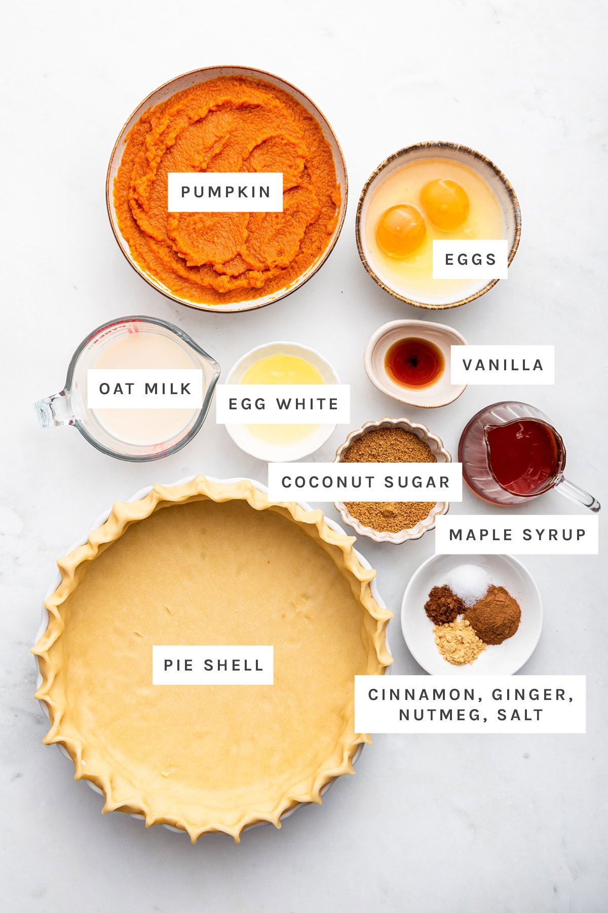 Ingredients measured out to make Healthy Pumpkin Pie: pumpkin, eggs, egg white, vanilla, oat milk, coconut sugar, maple syrup, pie shell, cinnamon, ginger, nutmeg and salt.