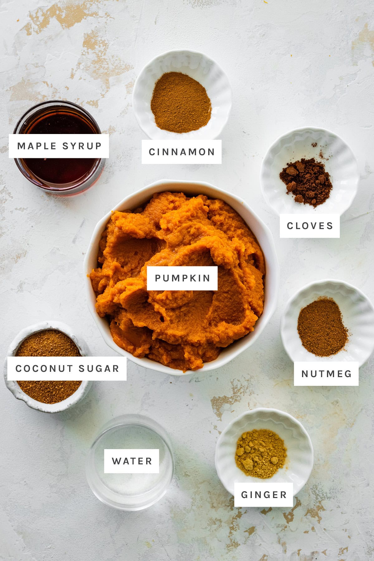 Ingredients measured out to make pumpkin butter: maple syrup, cinnamon, cloves, pumpkin, nutmeg, coconut sugar, water and ginger.