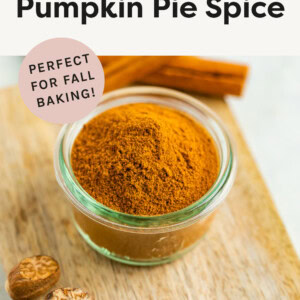 Homemade pumpkin pie spice in a glass jar on a little wooden cutting board next to some whole spices.