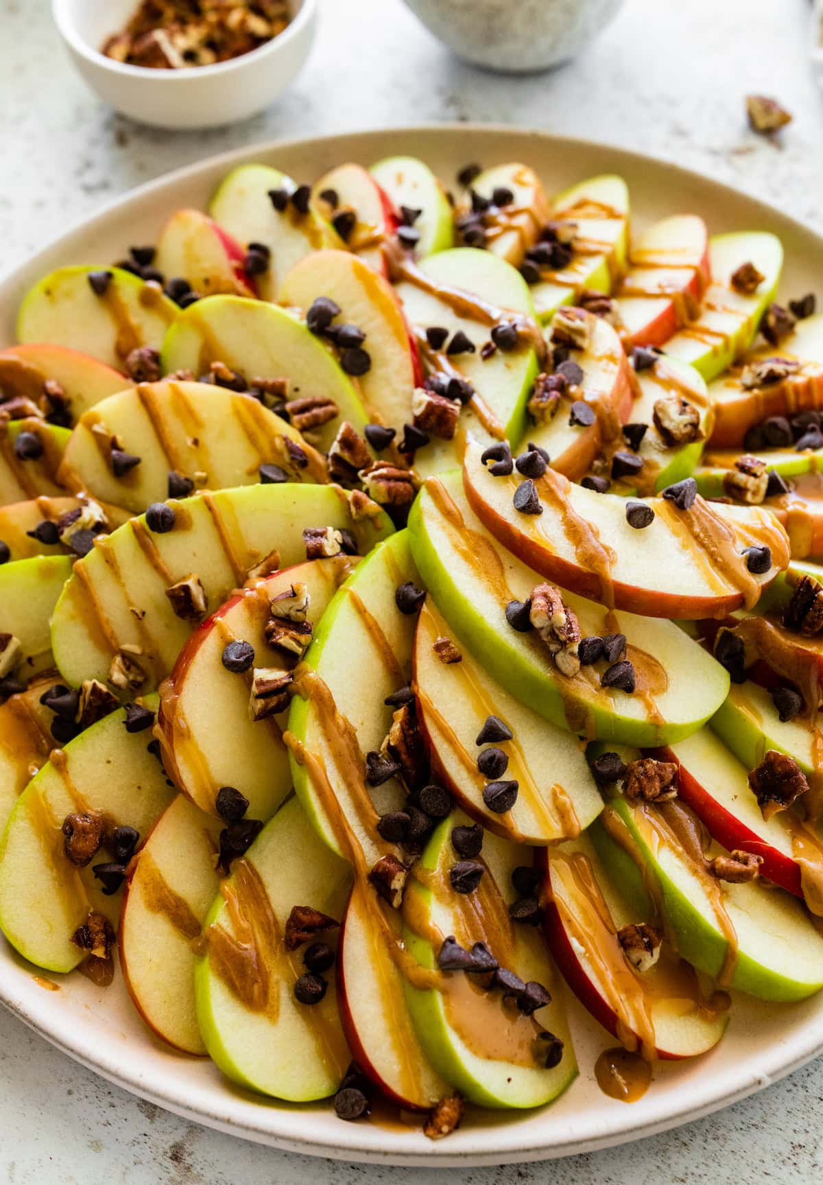 A large plate of apple nachos topped with a date caramel drizzle, mini chocolate chips, and pecans.