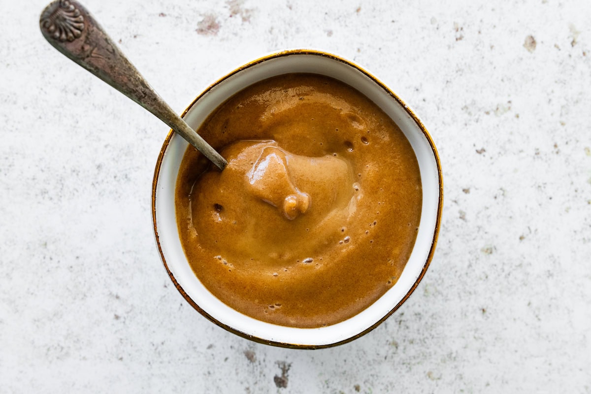 A date caramel sauce in a small bowl with a metal spoon inside the bowl.