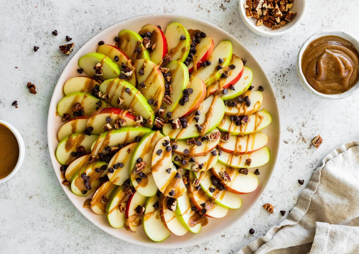 A large plate of apple nachos topped with a date caramel drizzle, mini chocolate chips, and pecans.