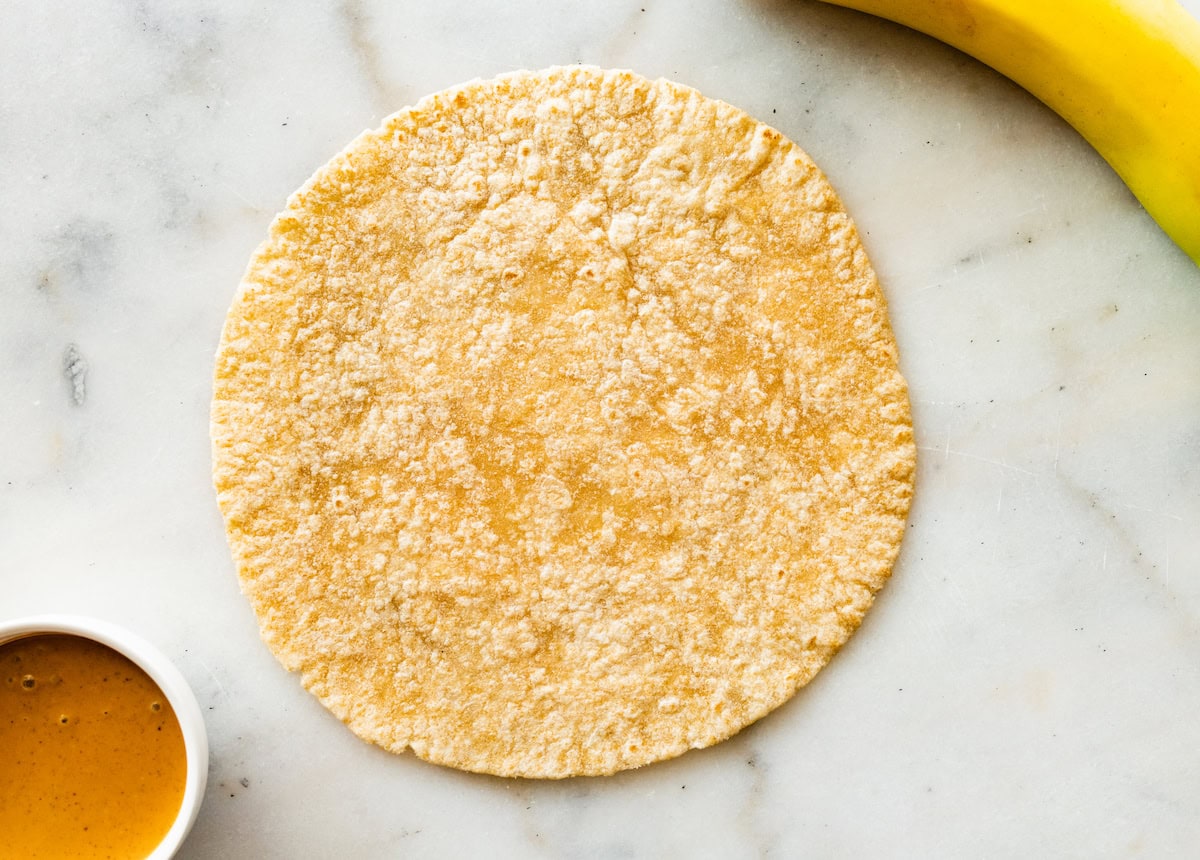 A whole wheat tortilla on a counter top that will be used for banana sushi roll ups.