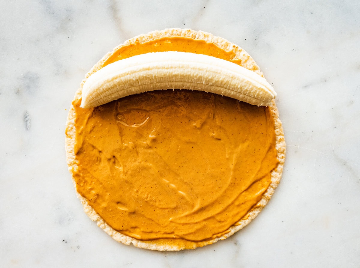 A whole wheat tortilla with nut butter spread and a banana on one side of the tortilla.