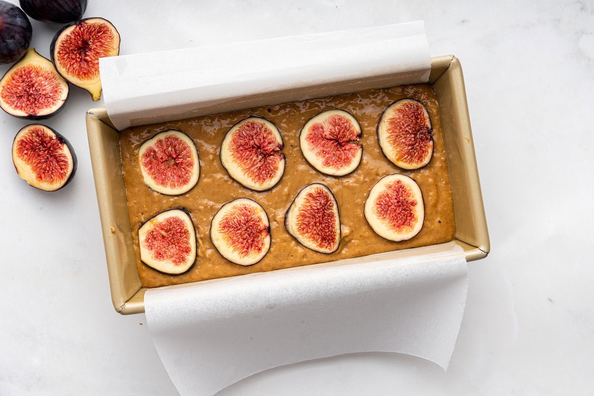 Fresh fig slices are added to the top of fig bread batter in a bread pan.