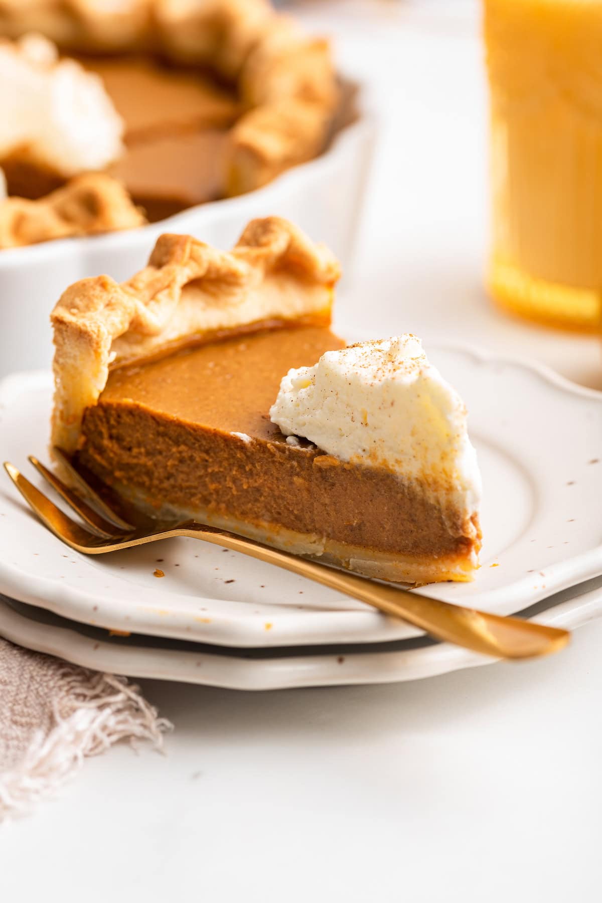 A slice of pumpkin pie on a plate with some whipped cream on top.
