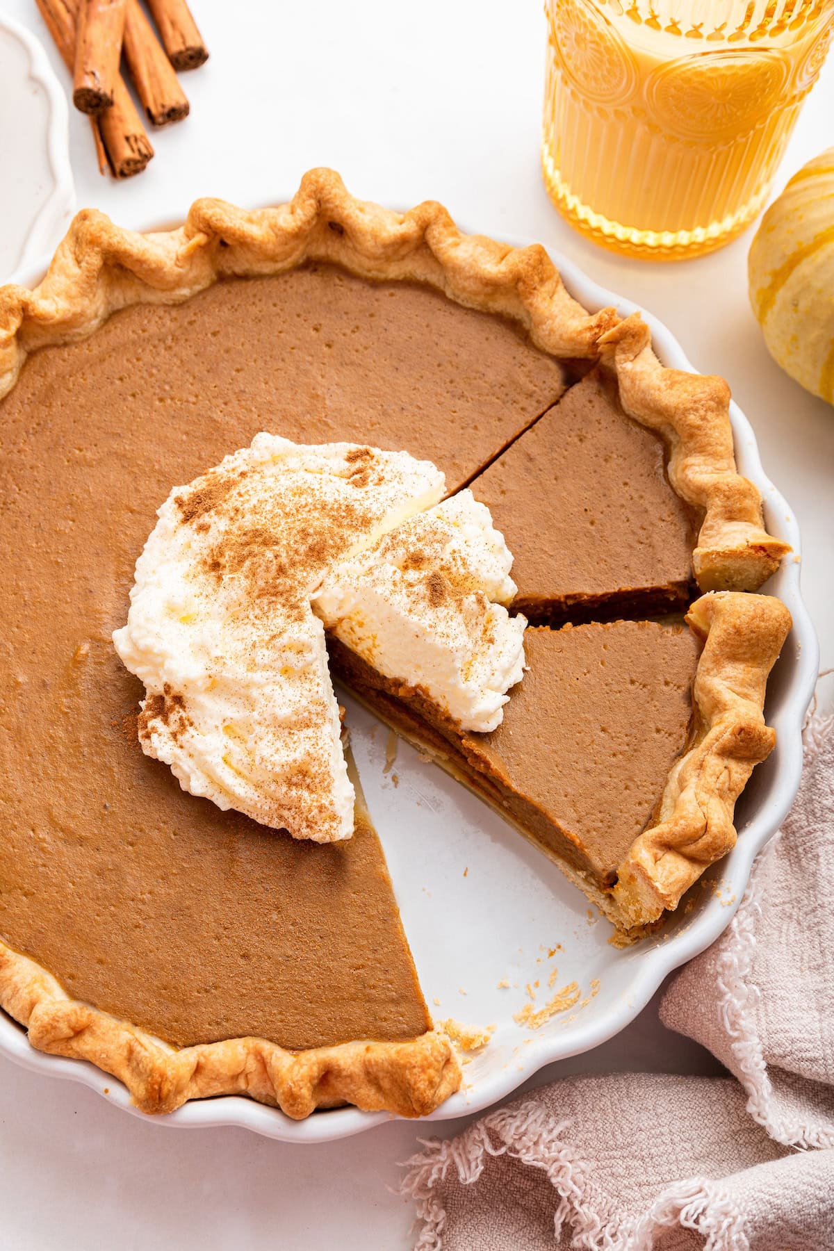 Healthy Pumpkin Pie topped with some whipped cream and cinnamon. A few slices are cut from the pie.