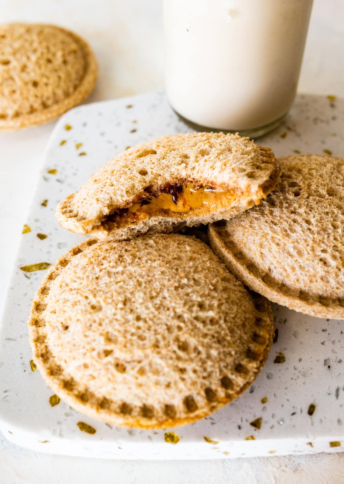 Three peanut butter uncrustables on a cutting board with one having a bite taken from it.