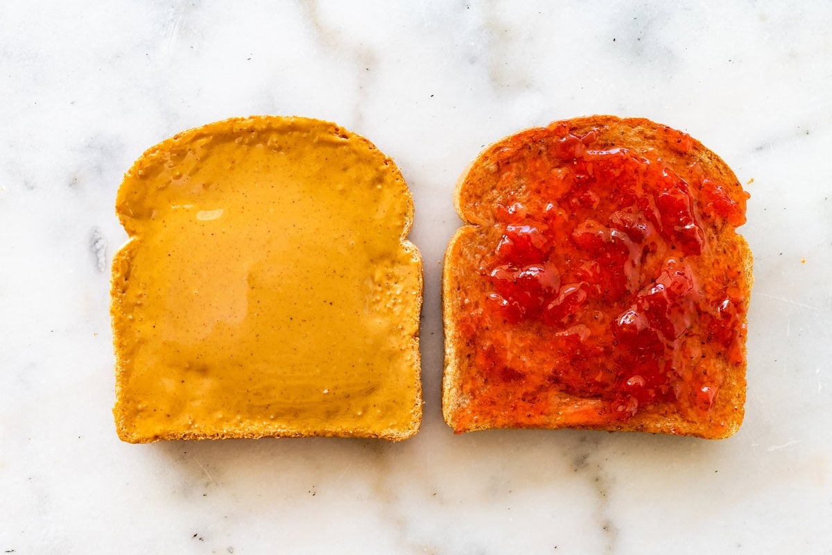 Two slices of bread, one with peanut butter, the other with a strawberry jam.