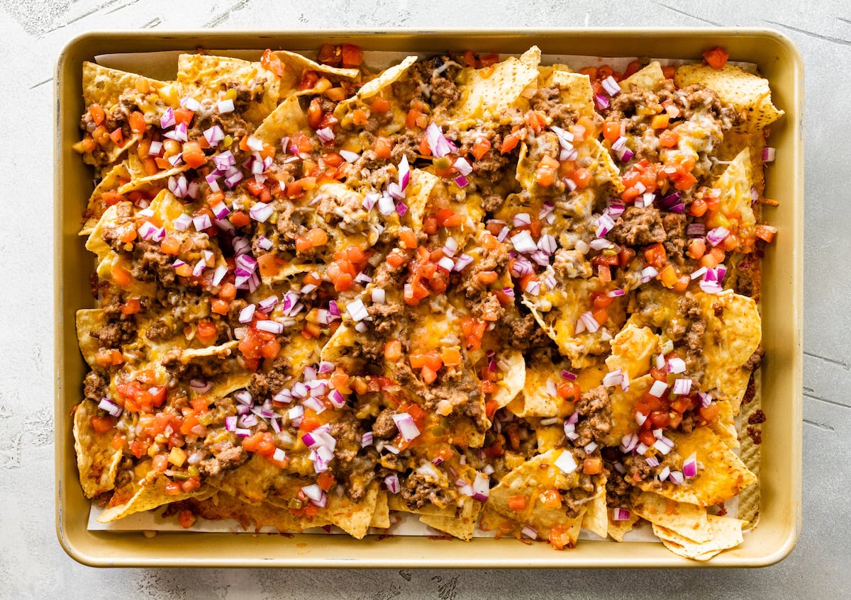 Loaded nachos on a baking tray with cheese, onion, tomato, meat, and beans.