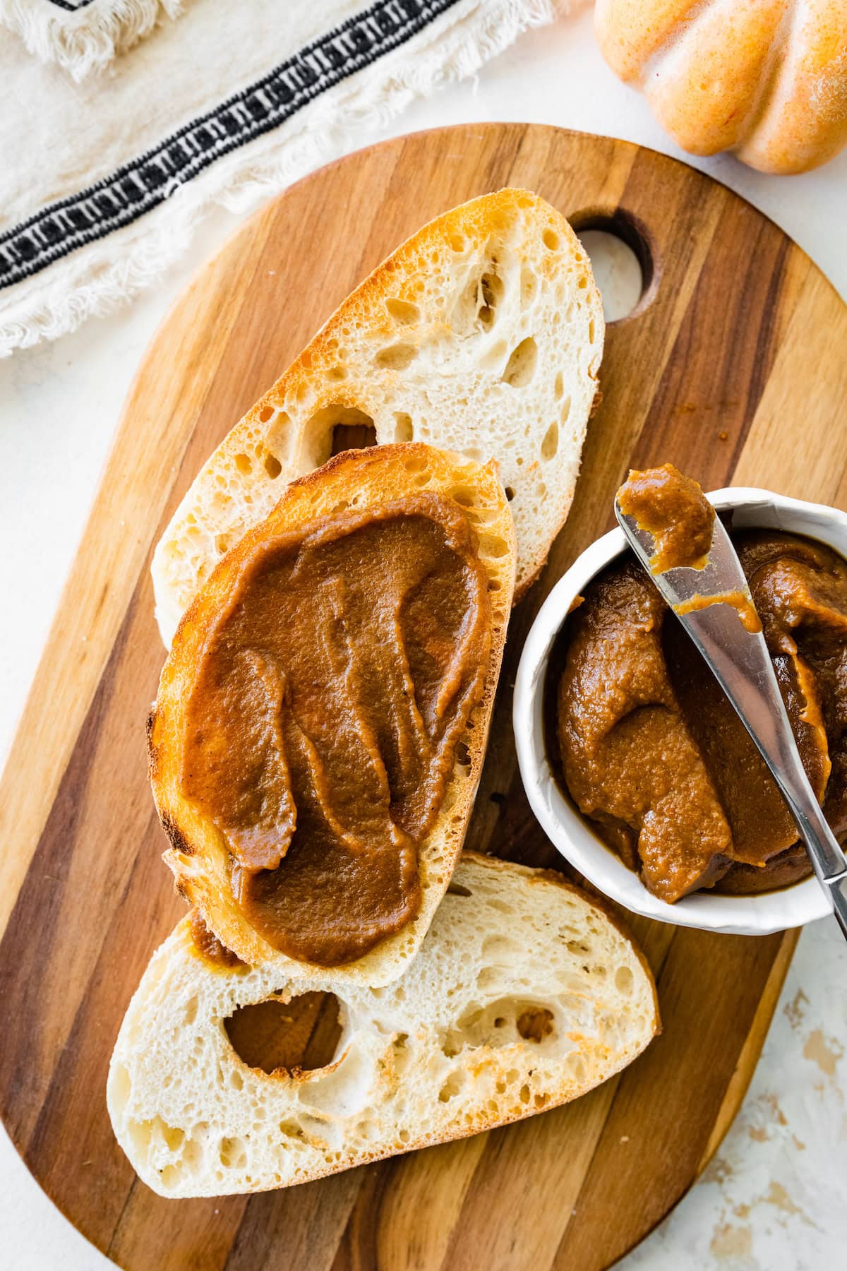 Three slices of bread on a cutting board with one slice having pumpkin butter spread on it.