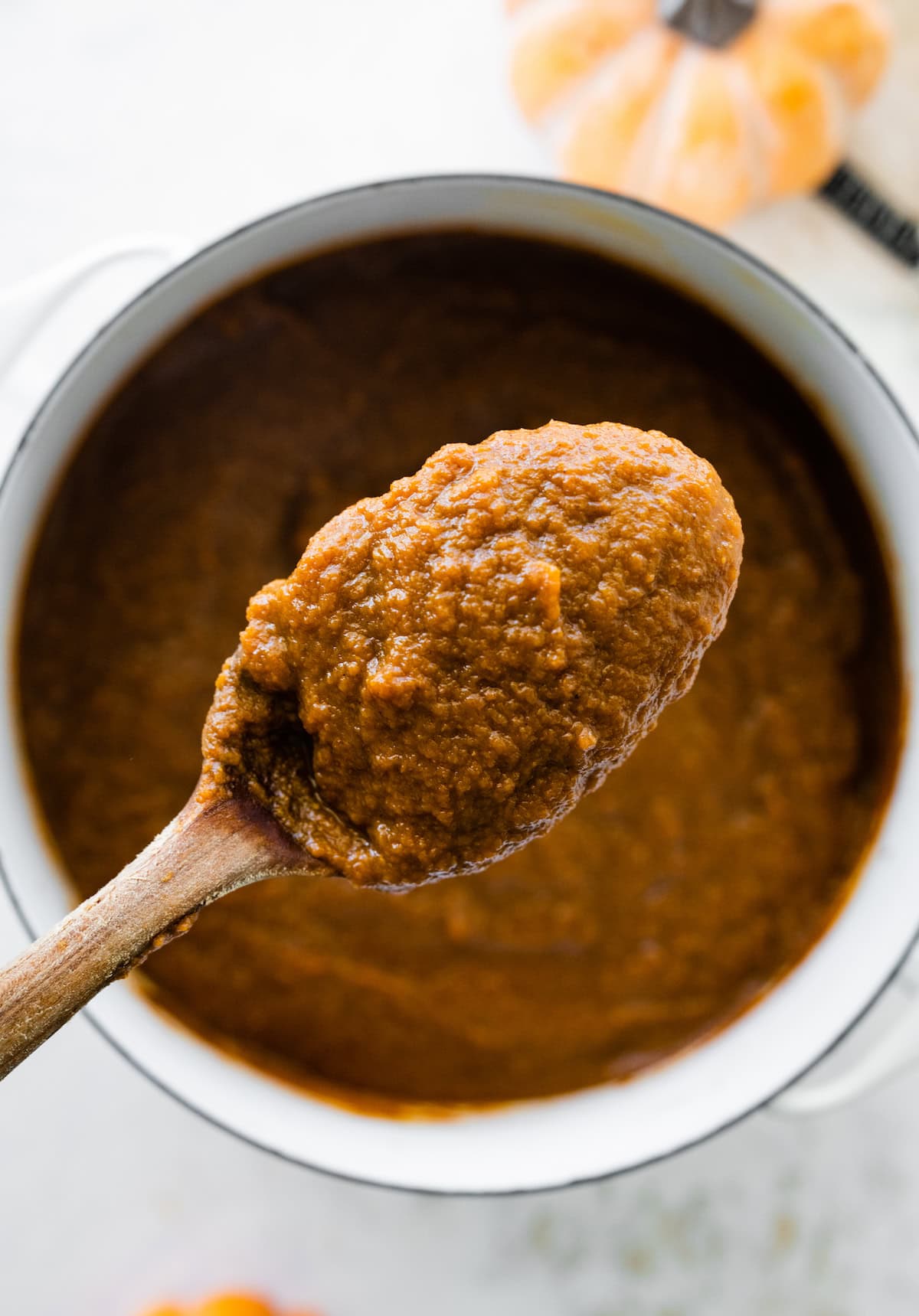 A spoonful of pumpkin butter over a pot of the pumpkin butter.