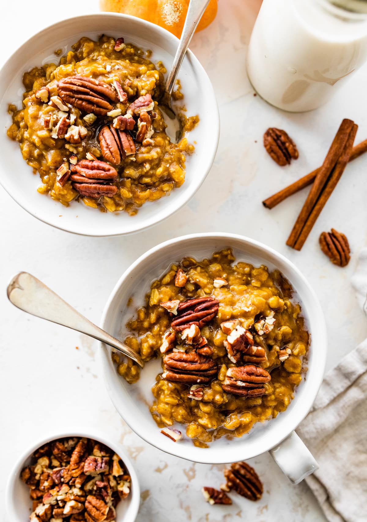 Two bowls of pumpkin oatmeal with milk and topped with pecans.