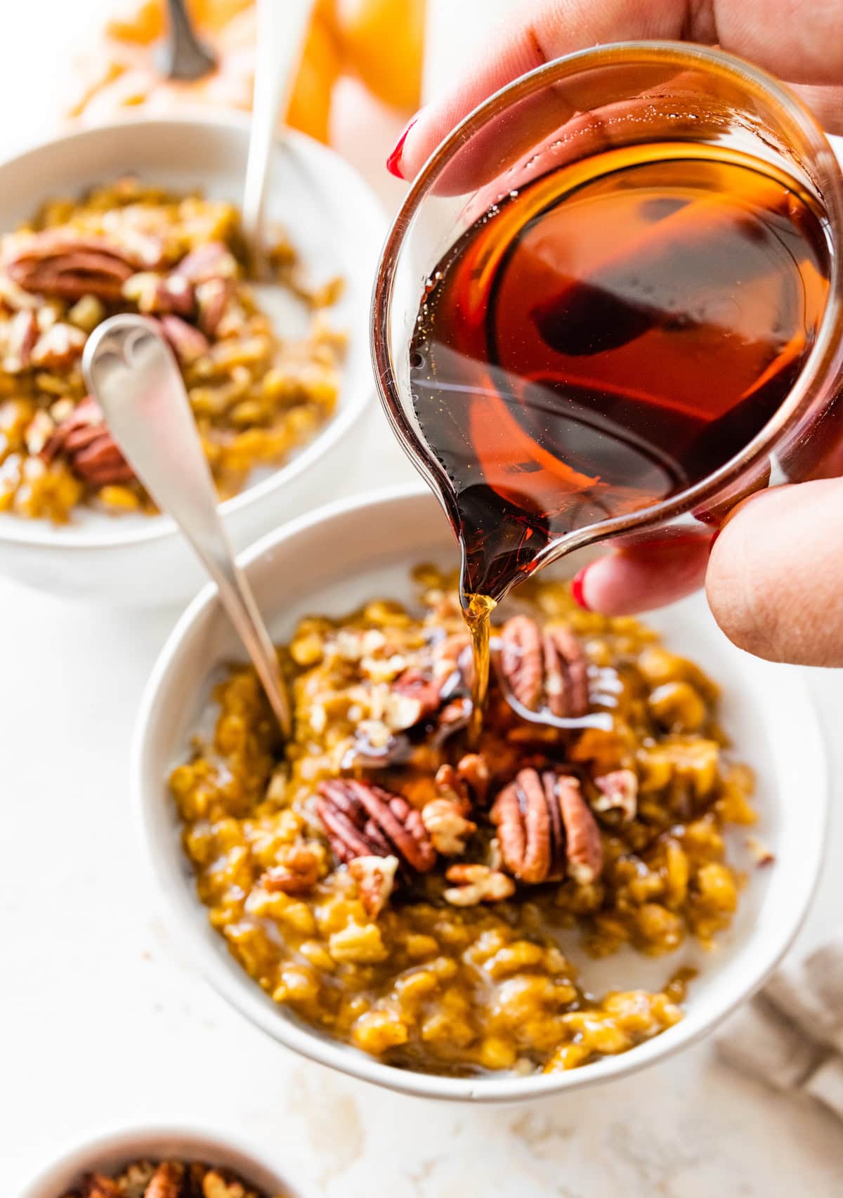 A woman's hand pours maple syrup into a bowl of pumpkin oatmeal.