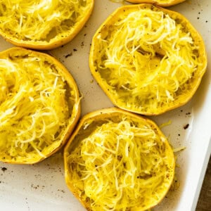 Roasted spaghetti squash rings in a white baking dish. The rings are shredded into long strands.