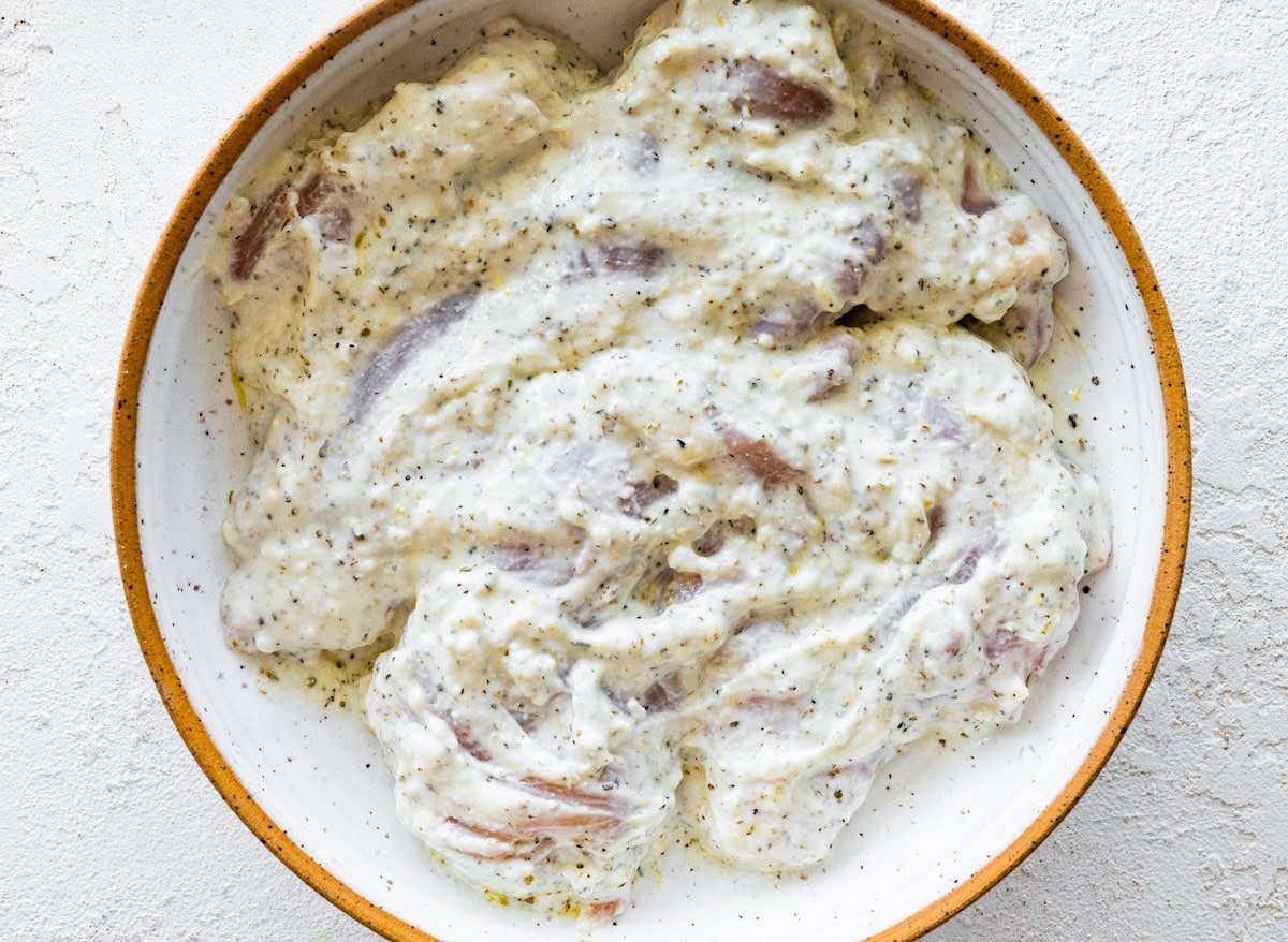 Raw chicken thighs marinating in a yogurt mix.