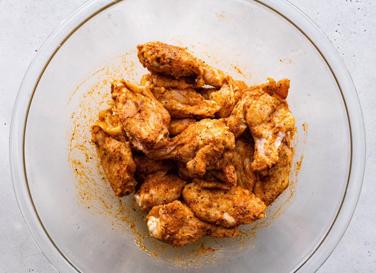 A large bowl of raw chicken wings coated in seasoning and oil.