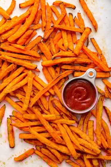Sweet potato fries spread out near a small container of ketchup.