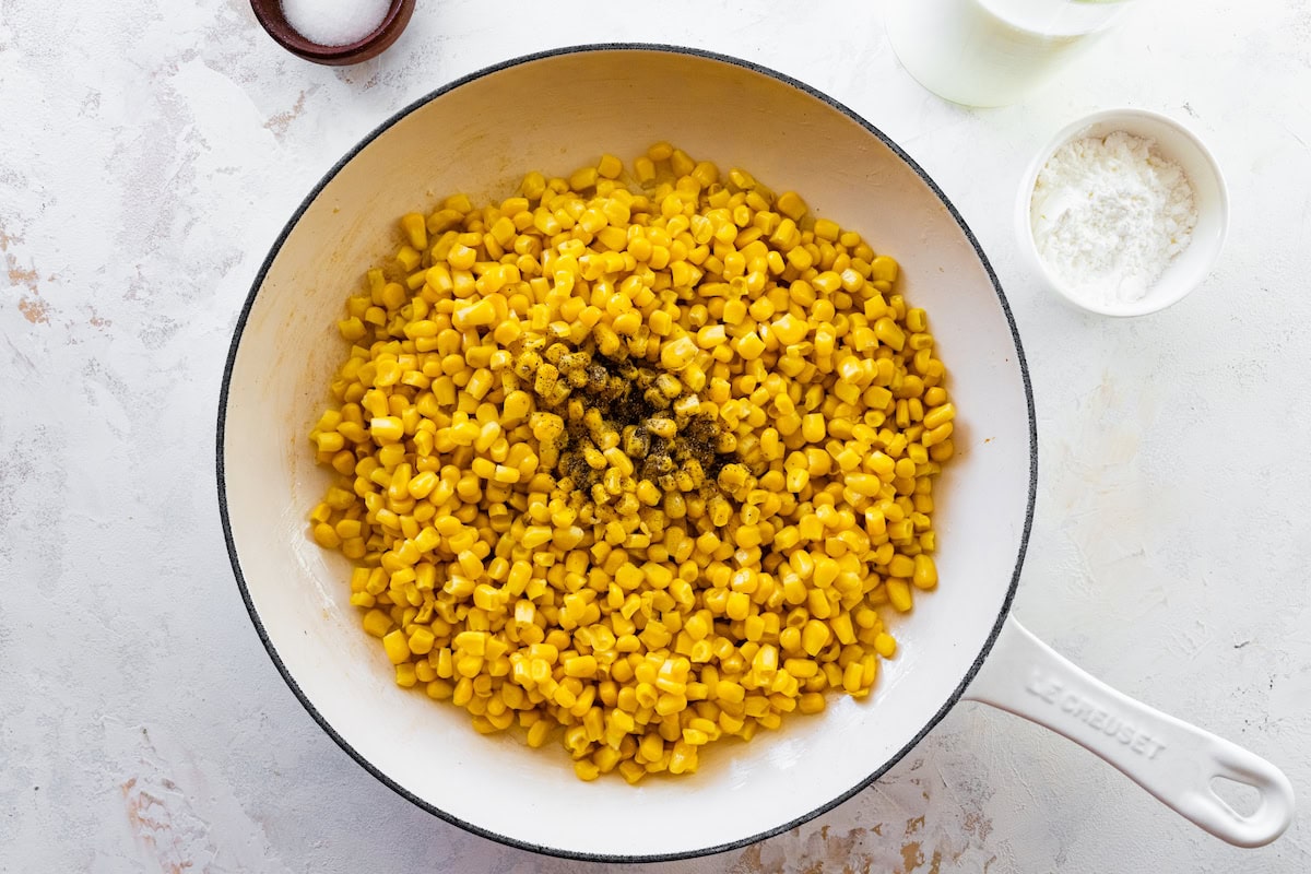 Corn and black pepper added to the white skillet with the chopped onions.