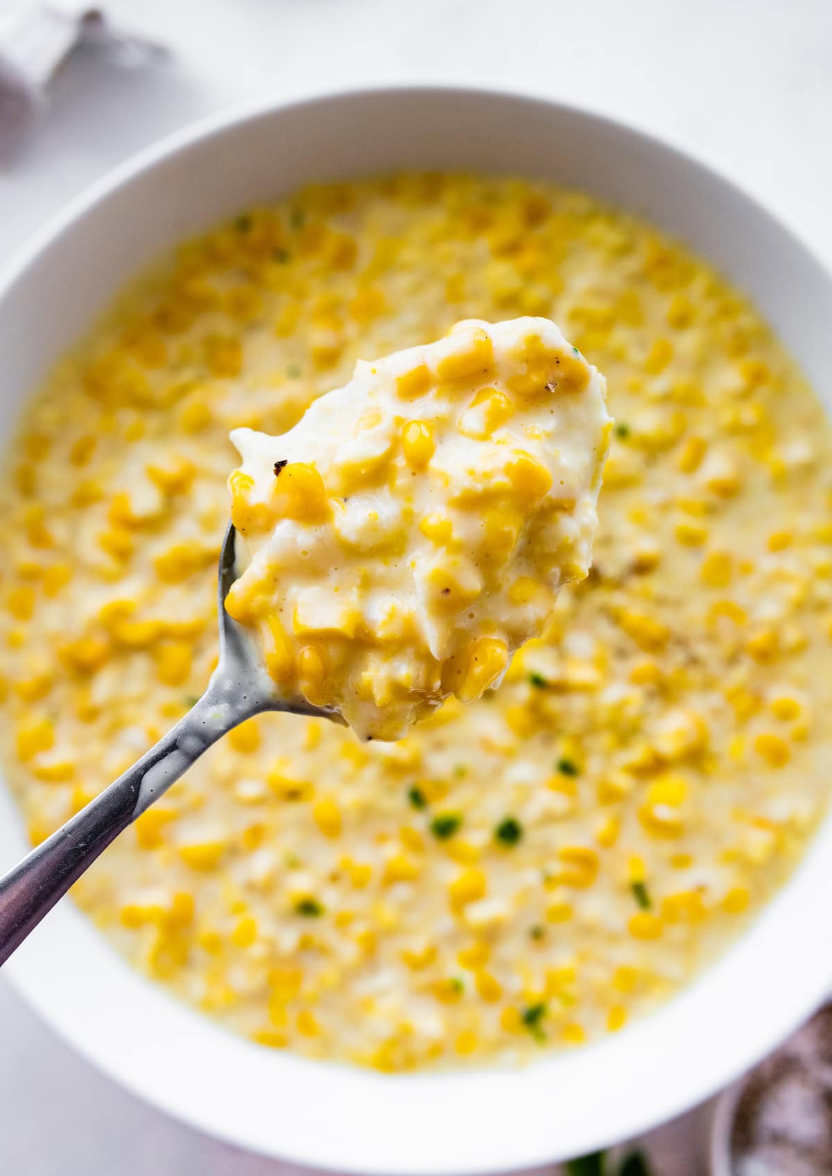 A silver spoon scooping a bite of the creamed corn from a white bowl.