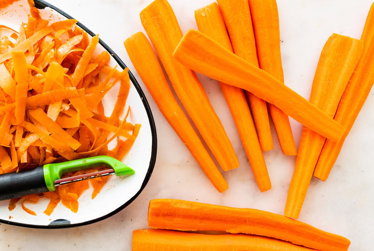 Multiple peeled carrots on a counter top near a peeler.