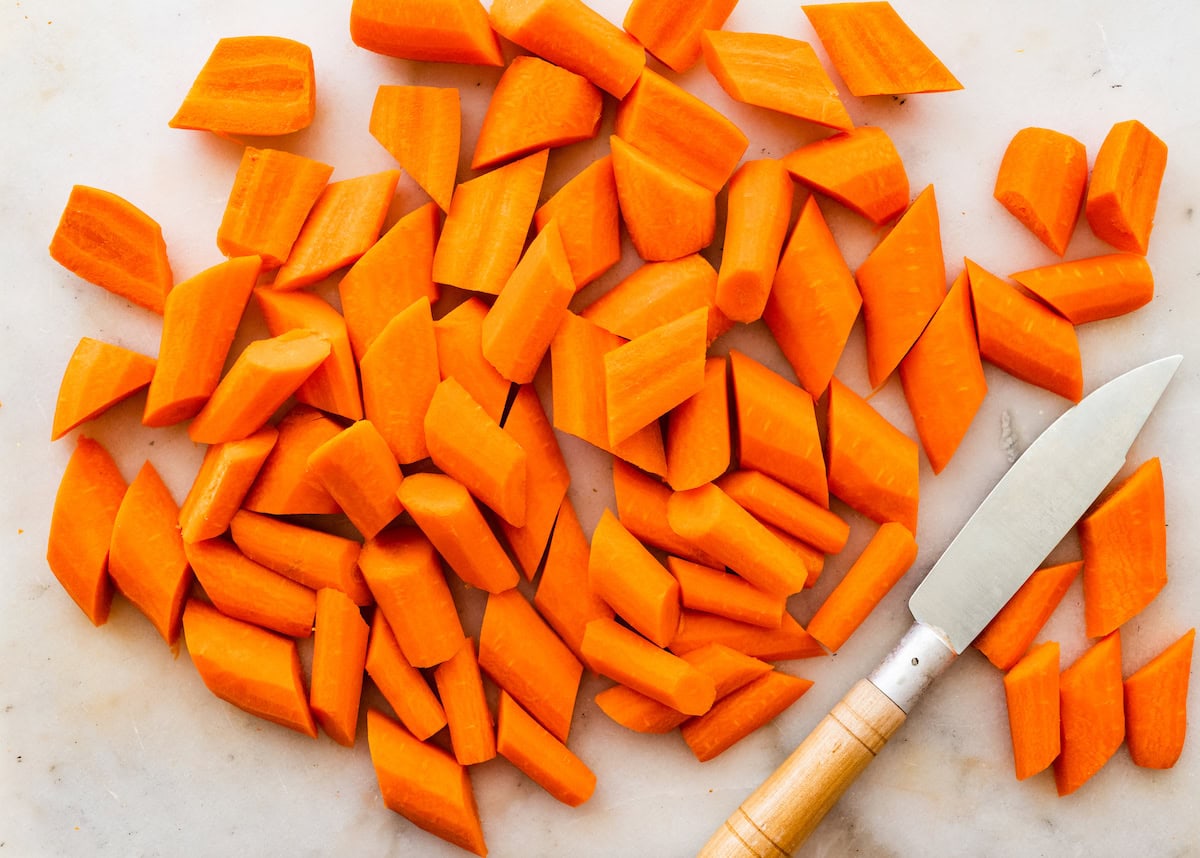 A knife near many chopped carrots.
