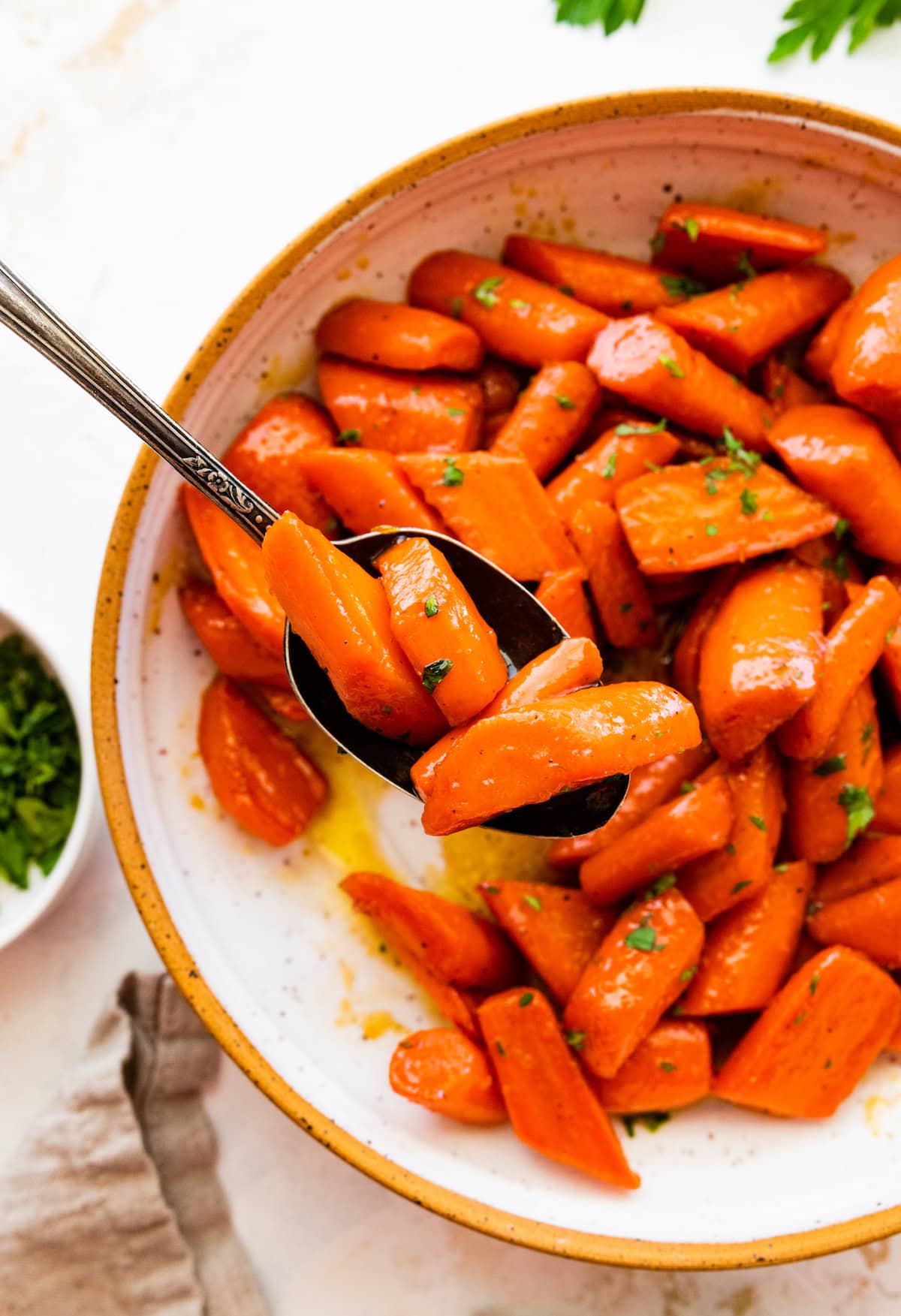 A spoonful of glazed carrots over a plate of the carrots.