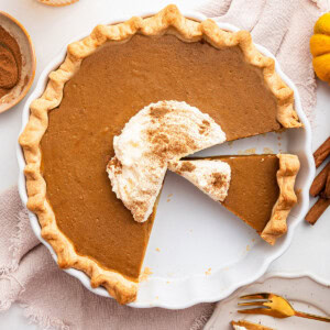 Healthy Pumpkin Pie topped with some whipped cream and cinnamon. A few slices are cut from the pie.