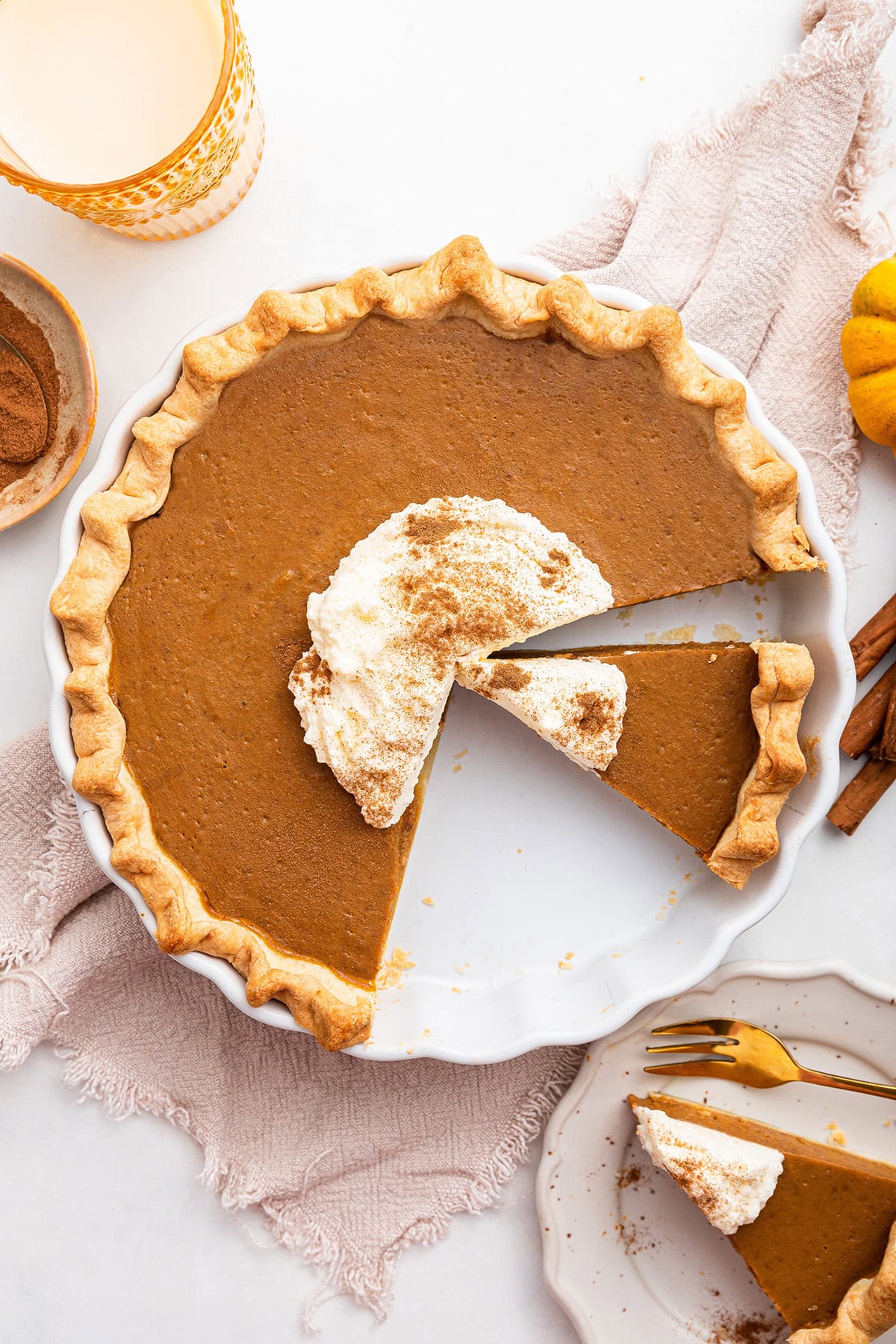 Healthy Pumpkin Pie topped with some whipped cream and cinnamon. A few slices are cut from the pie.