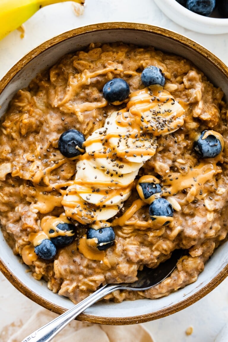 A serving of peanut butter oatmeal in a bowl topped with sliced banana, fresh blueberries, chia, and a drizzle of peanut butter.