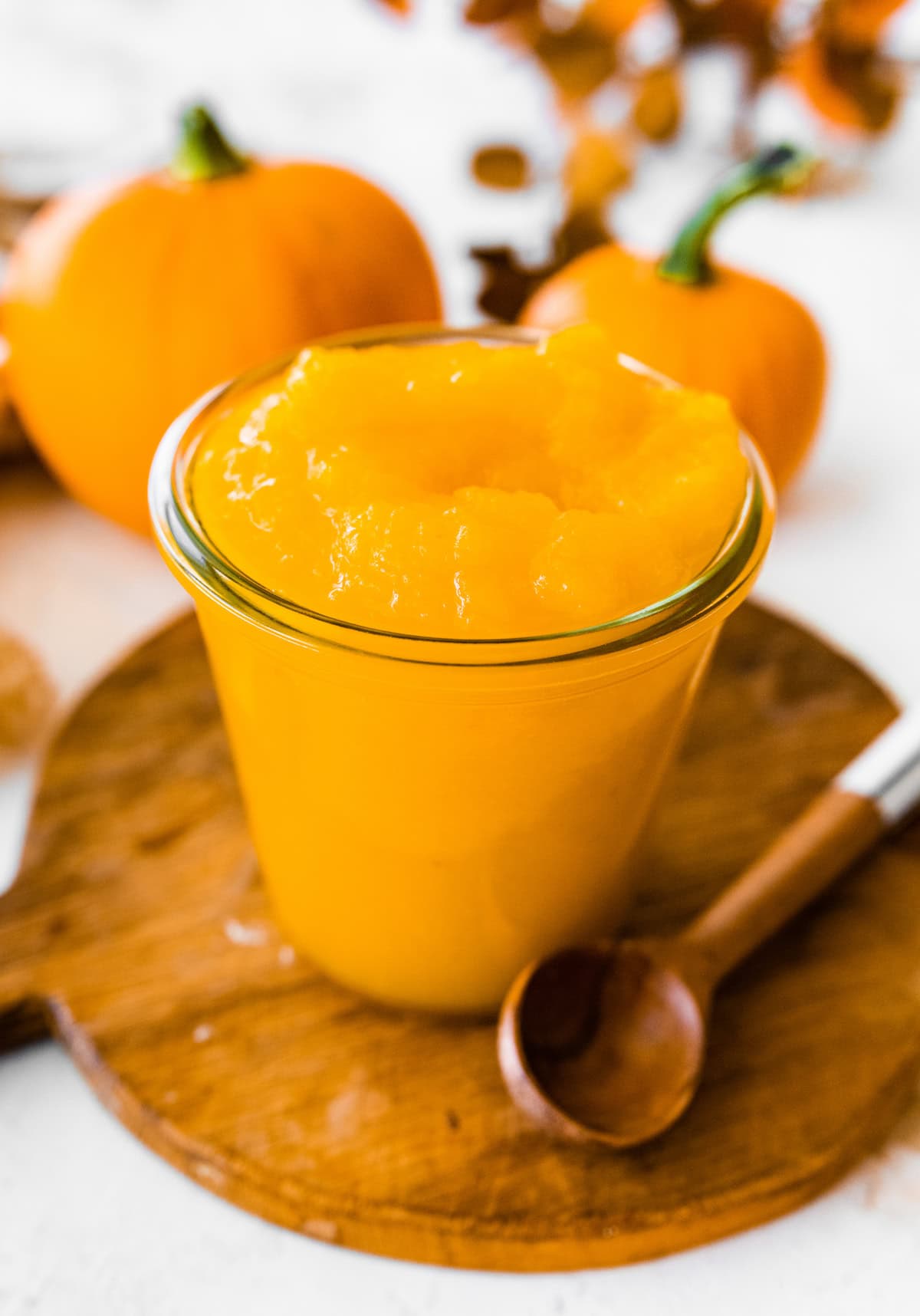 A homemade pumpkin puree in a glass jar on a circular wooden board.