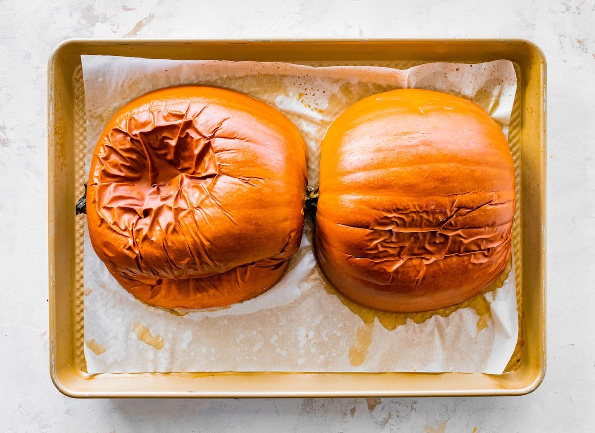 Two halves of a small pumpkin on a baking tray after being baked in the oven.
