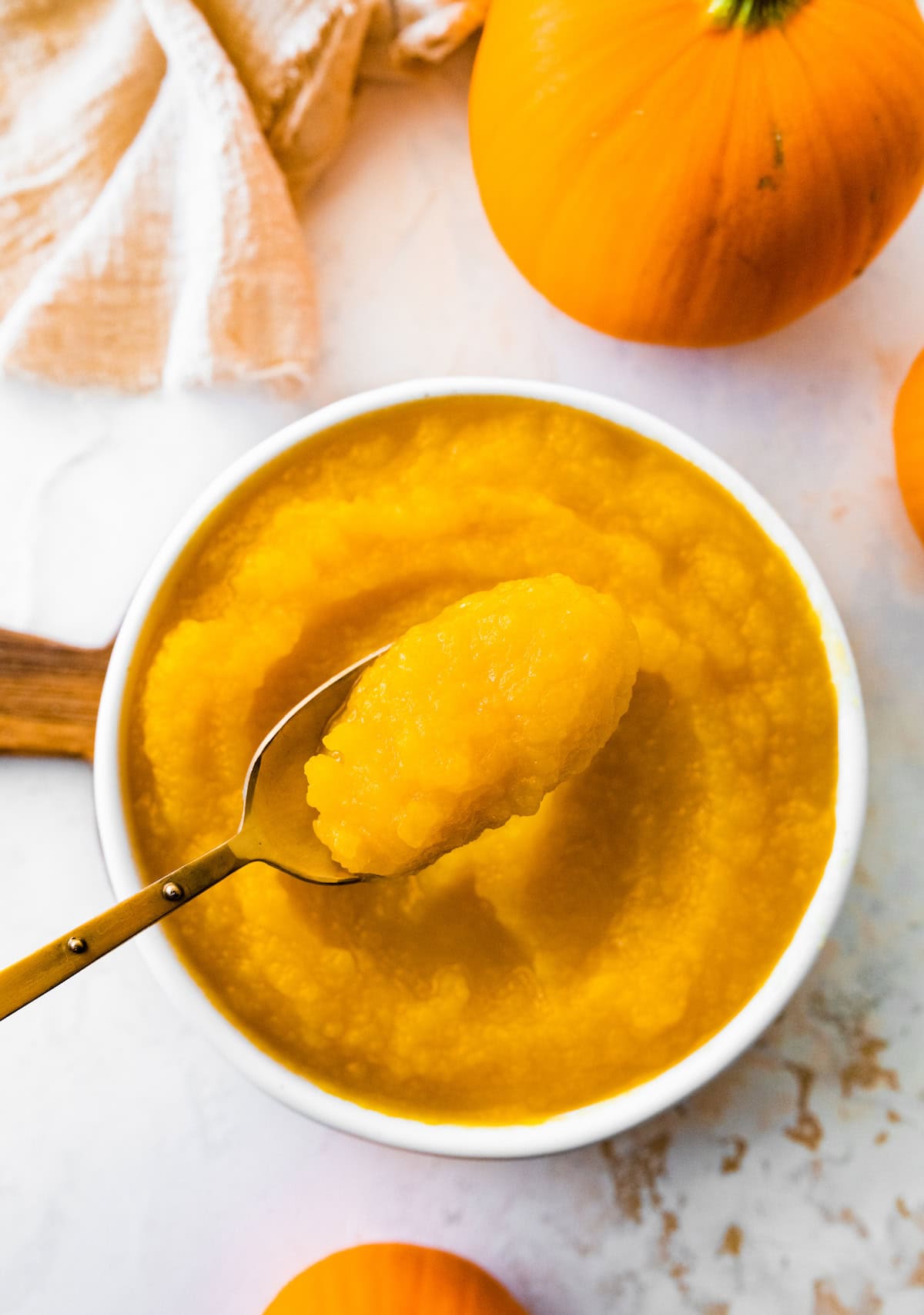A homemade pumpkin puree on a spoon that is being held over a bowl of the puree.