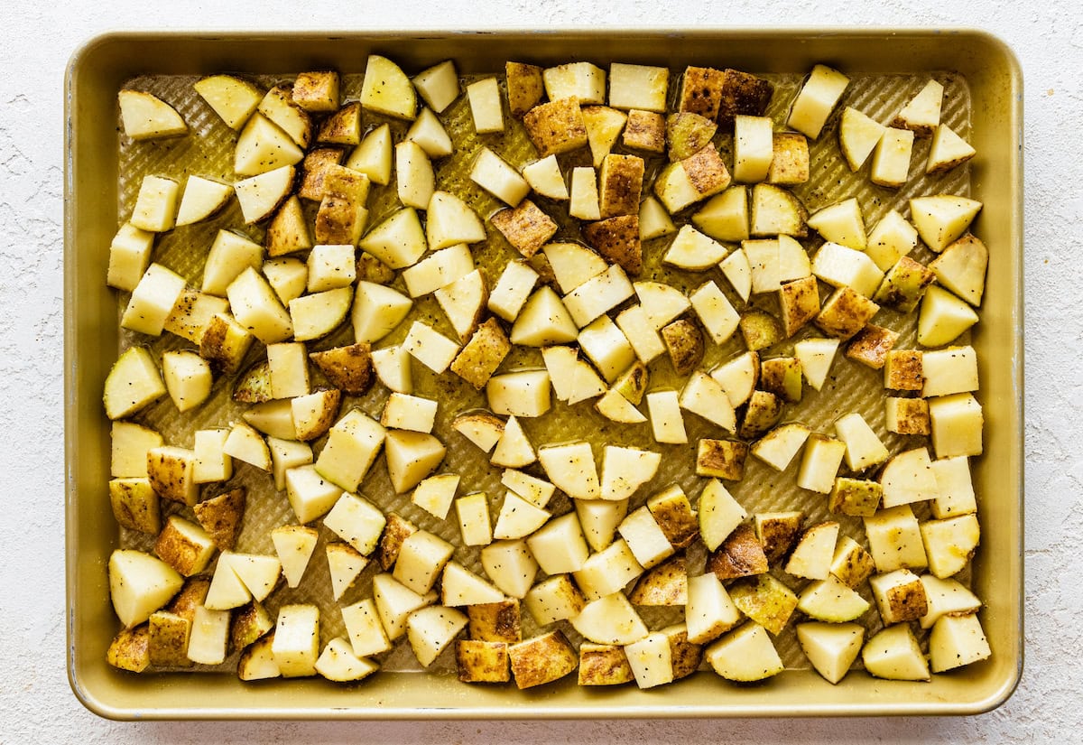 A baking tray of seasoned potatoes cut into chunks.