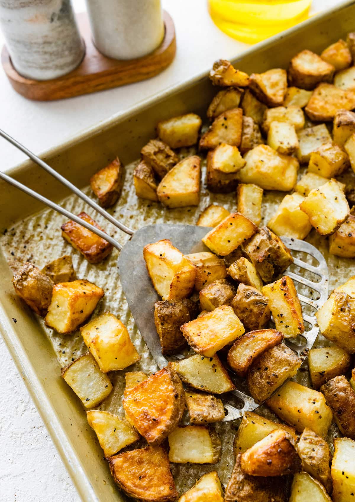 Roasted potato chunks on a baking tray with a metal spatula.